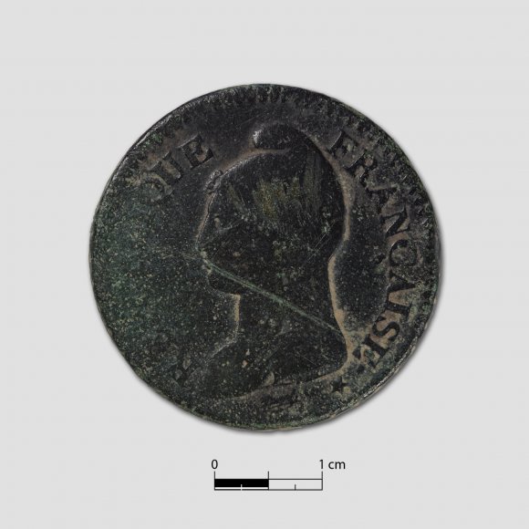 1 Centime - „Un Decime Republique Francaise“<br>
Eine Münzprägung aus der Revolutionszeit. L’An 7 weißt auf das siebte Jahr nach dem französischen Revolutionskalender hin. Aufgeprägt ist ein Mann mit phrygischer Mütze (auch Jakobinermütze). Die Jakobiner waren eine radikale Bewegung der Französischen Revolution. (⌀ 31 mm; Gewicht: 19,6 g)